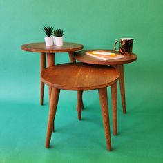 two small wooden tables sitting on top of a green floor next to a cup and plant