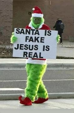 the grinch is holding a sign that says santa is fake jesus is real