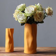 two yellow vases with white flowers in them on a wooden table next to each other