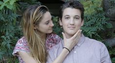 a young man and woman standing next to each other in front of some trees with their hands together