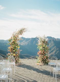 an outdoor ceremony setup with white chairs and flowers on the arch, surrounded by mountains