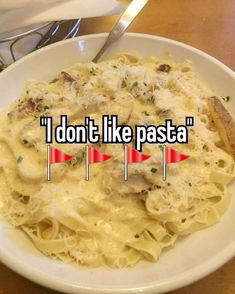 a white bowl filled with pasta on top of a wooden table next to a fork and knife