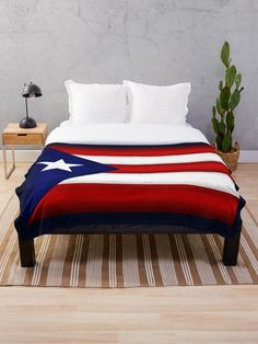 a bed with a red, white and blue blanket on it next to a potted plant