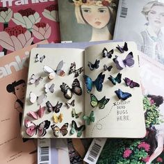 an open book with lots of butterflies on top of it next to magazines and magazines