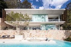 a modern house with a pool in the foreground and stone walls on the other side