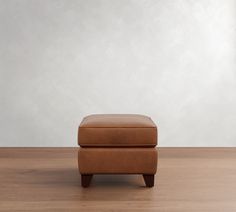 a brown foot stool sitting on top of a wooden floor next to a white wall