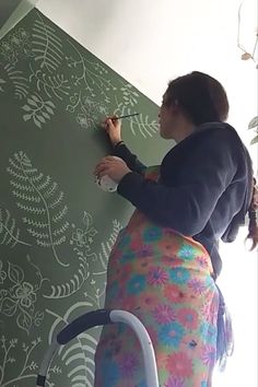 a woman is writing on the wall with a marker and paint roller in front of her