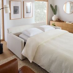 a bed with white sheets and pillows in a bedroom next to a large window that has pictures on the wall above it