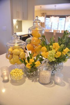 a table topped with vases filled with yellow flowers and lemons next to candy