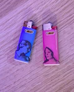 two lighters sitting on top of a wooden table next to each other, one with a woman's face painted on it