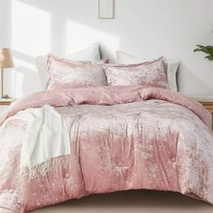 a bed with pink comforter and pillows in a room next to a lamp on a table