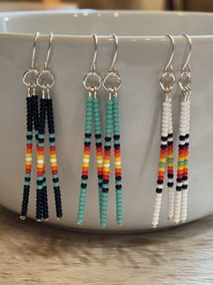 three pairs of beaded earrings hanging from hooks on a white bowl with a wooden table in the background