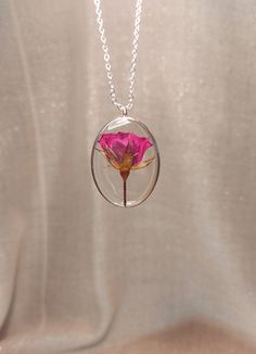 a necklace with a pink flower inside of it on a silver chain hanging from a white background