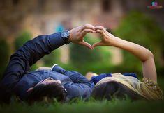 two people laying in the grass making a heart shape with their hands while holding each other