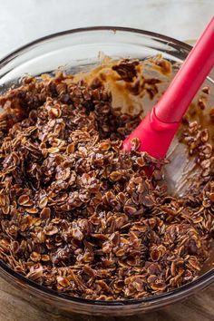 a glass bowl filled with granola on top of a wooden table next to a red spatula