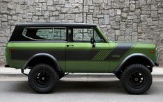 a green and black truck parked in front of a stone wall