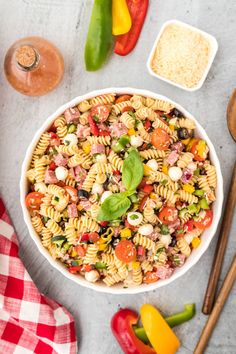 a bowl filled with pasta salad on top of a table next to vegetables and seasoning