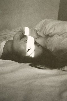 a woman laying on top of a bed next to a white pillow and blanket with a lit candle in her mouth