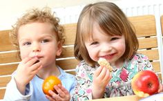 two children sitting at a table eating fruit