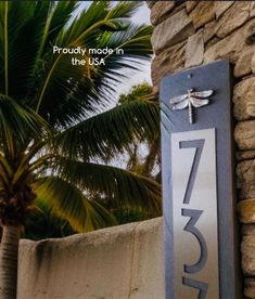 a house number sign with a dragonfly on it and palm trees in the background