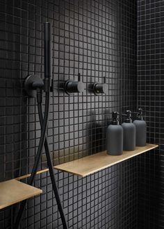 a bathroom with black tiled walls and shelves holding soap dispensers, shower heads and faucets