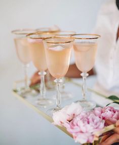 a tray topped with glasses filled with champagne and pink peonies on top of it