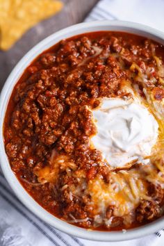 a white bowl filled with chili and cheese on top of a table next to tortilla chips