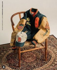 a baseball jacket sitting on top of a wooden chair next to a hat and glove