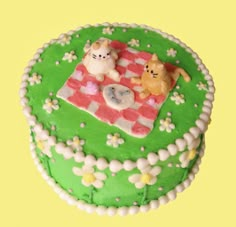 there is a green cake with white frosting on the top and two small bears sitting at a picnic table