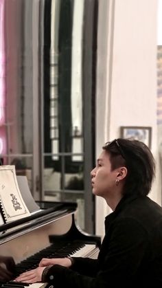 a young man sitting at a piano in front of a mirror with his head turned to the side