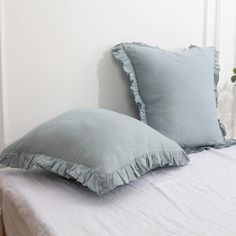 two light blue pillows sitting on top of a white bed next to a potted plant