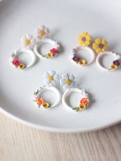 four rings with flowers on them sitting on a white plate next to a wooden table