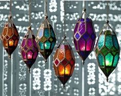 five colorful lights hanging from hooks on a white and gray wall with geometric patterns in the background