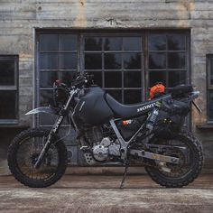 a black motorcycle parked in front of an old building with broken windows and dirt on the ground