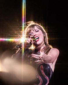 a woman singing into a microphone while holding her hands out to the side with lights in the background