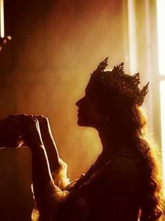 a woman with long hair wearing a crown and holding something in her hand while standing next to a window