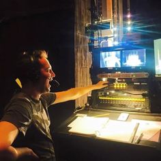 a man sitting in front of a mixing desk with headphones on and pointing at the screen