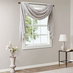 a living room with white walls and a window covered in sheer drapes on the windowsill