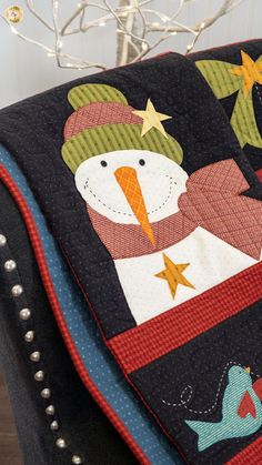 a snowman quilted on the back of a chair with christmas lights in the background