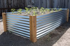 a raised garden bed with plants growing in the top and bottom part, along side a wooden fence