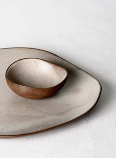 a white plate with a wooden bowl on it's side, sitting on a table