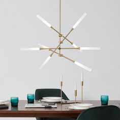 a modern chandelier hanging over a dining room table with green chairs and place settings