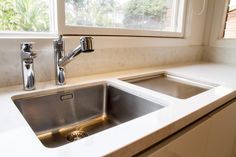 a stainless steel sink and faucet in a white countertop with a window