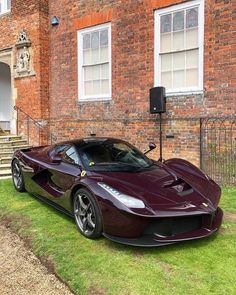 a maroon sports car parked in front of a brick building with stairs leading up to it