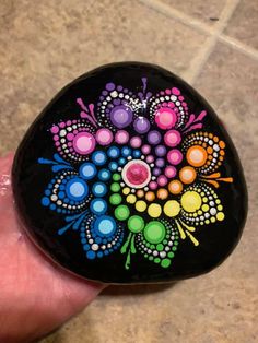 a hand holding a black rock with colorful designs on it