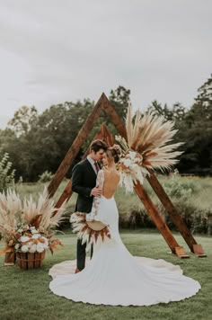 a bride and groom standing in front of an arch made out of wooden sticks with dried flowers