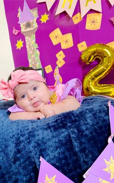 a baby laying on top of a blue blanket next to a number 2 sign and balloons