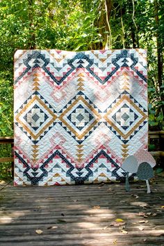 a quilt on a wooden deck with trees in the background