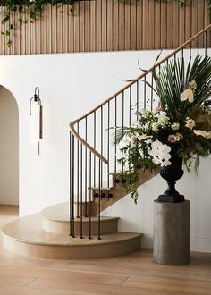 an elegant staircase with flowers and greenery on the bannister railing, in front of a white wall