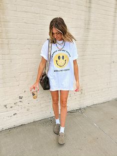 a woman is walking down the sidewalk wearing a smiley face t - shirt